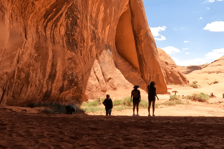 Three people standing in a large, sunlit sandstone cave entrance.