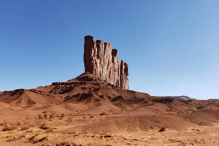 Tall rocky formation in a desert landscape under a clear blue sky.