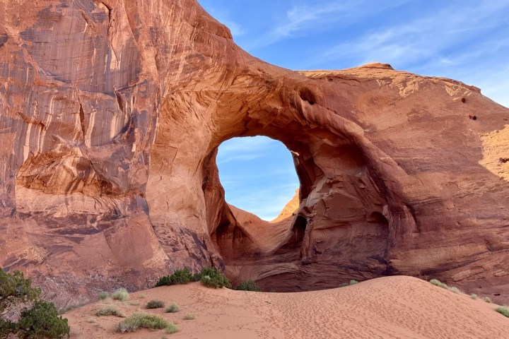 A large natural rock arch in a desert landscape under a blue sky.