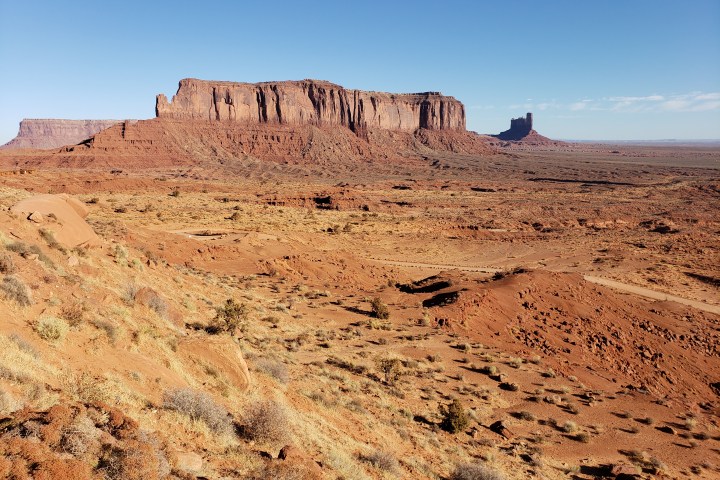 Desert landscape with red rock mesa and clear blue sky in the background.