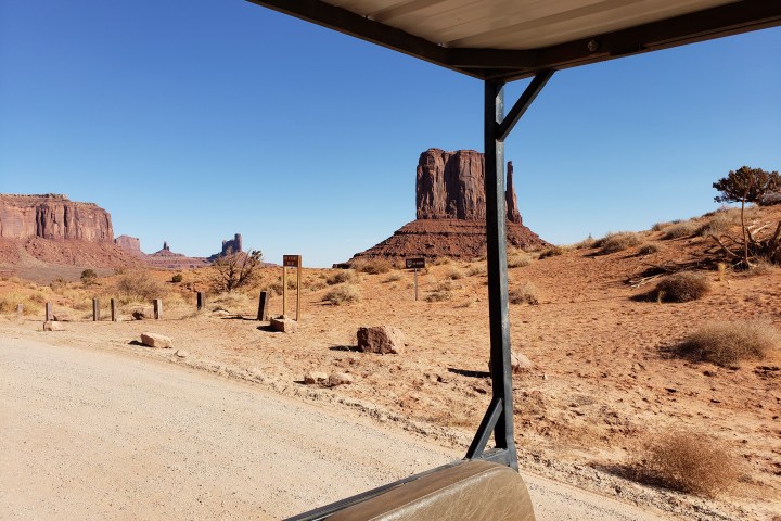 Desert landscape with red rock formations under a clear blue sky, viewed from a covered vehicle.