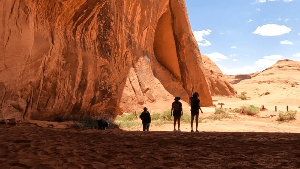 Four people silhouetted against a large red rock formation and blue sky.
