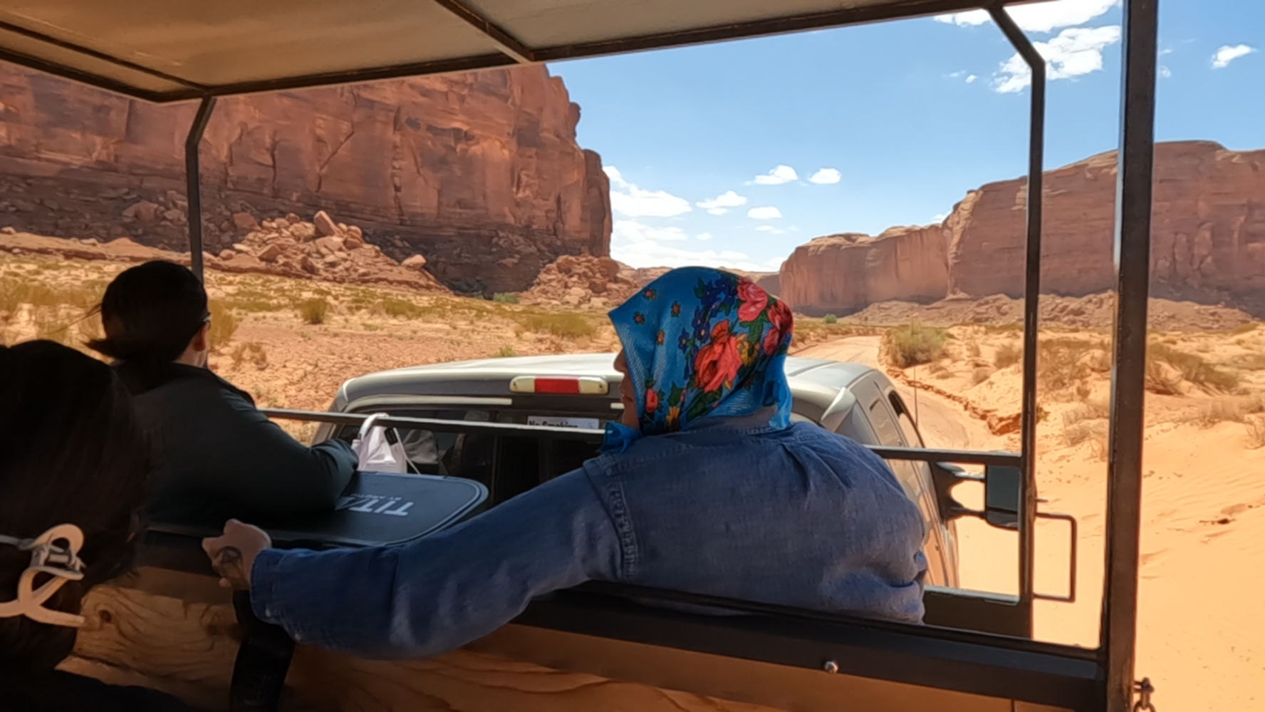 Two people in a vehicle touring a rocky desert landscape with cliffs.
