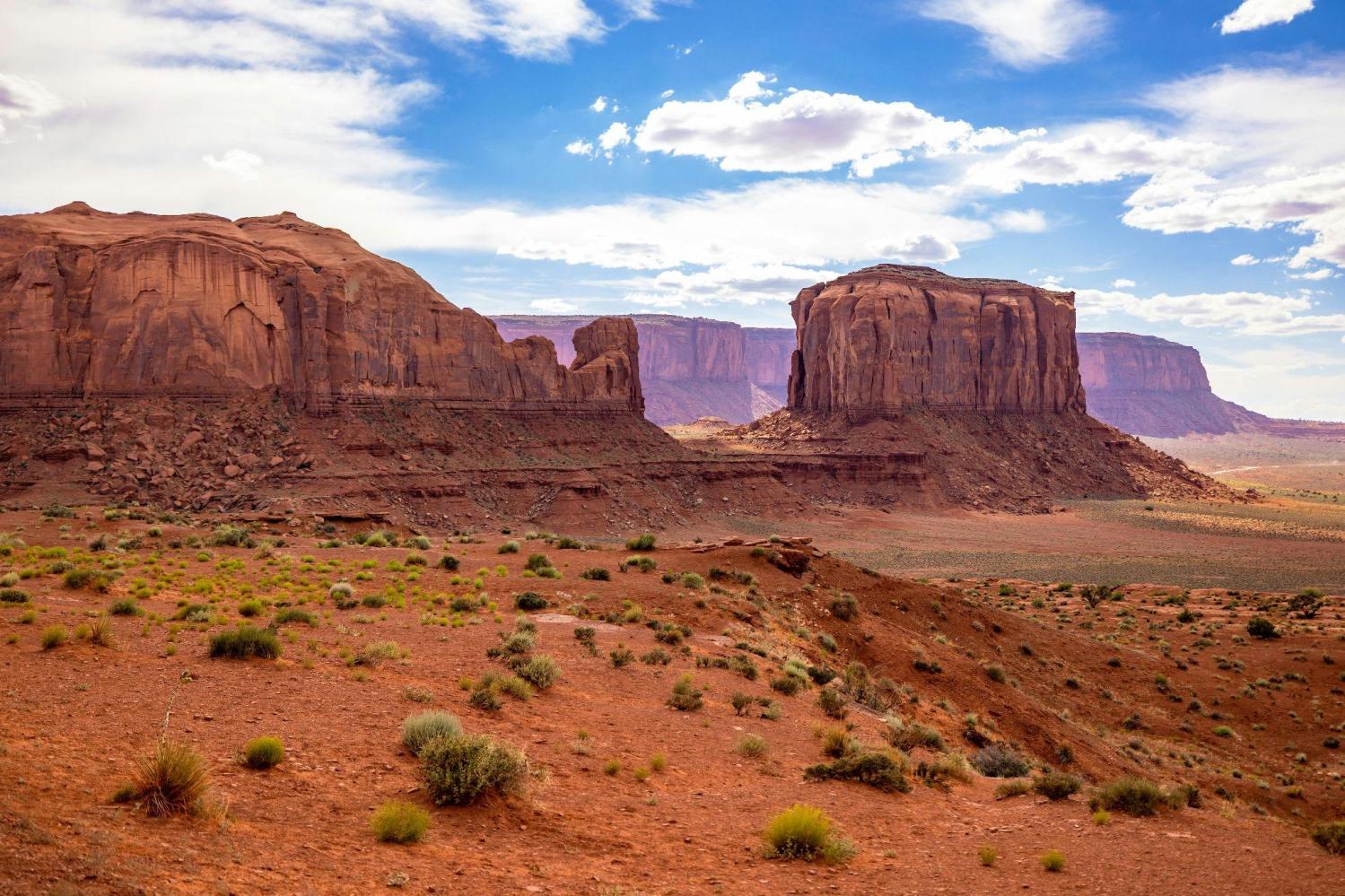 Desert landscape with large rock formations under a blue sky with clouds.