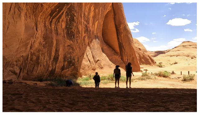 Four people walking along a rocky canyon in bright sunlight.