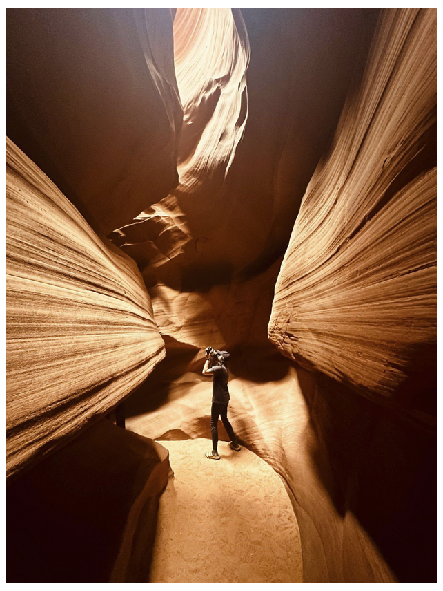 Person in narrow sandstone canyon taking a photo upwards.