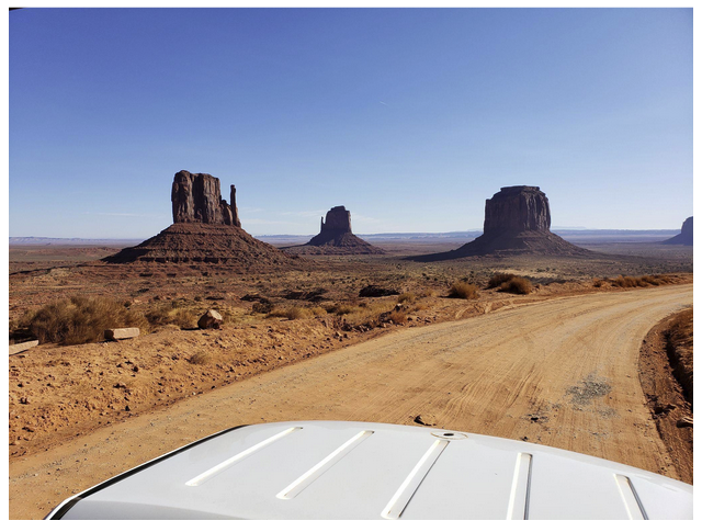 Desert landscape with rock formations under clear sky, vehicle roof visible in foreground.