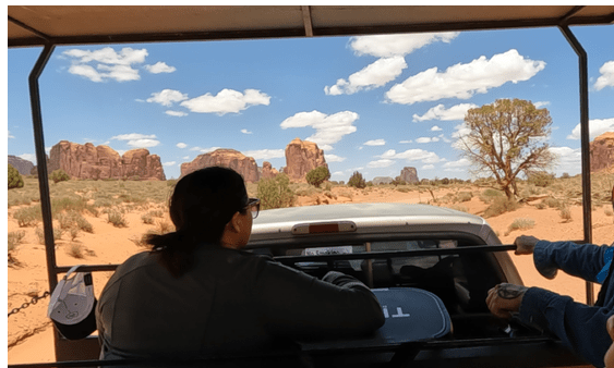 People on a desert tour vehicle, view of rock formations and blue sky with clouds.