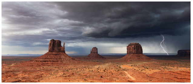 Desert landscape with rock formations, dark clouds, and lightning.