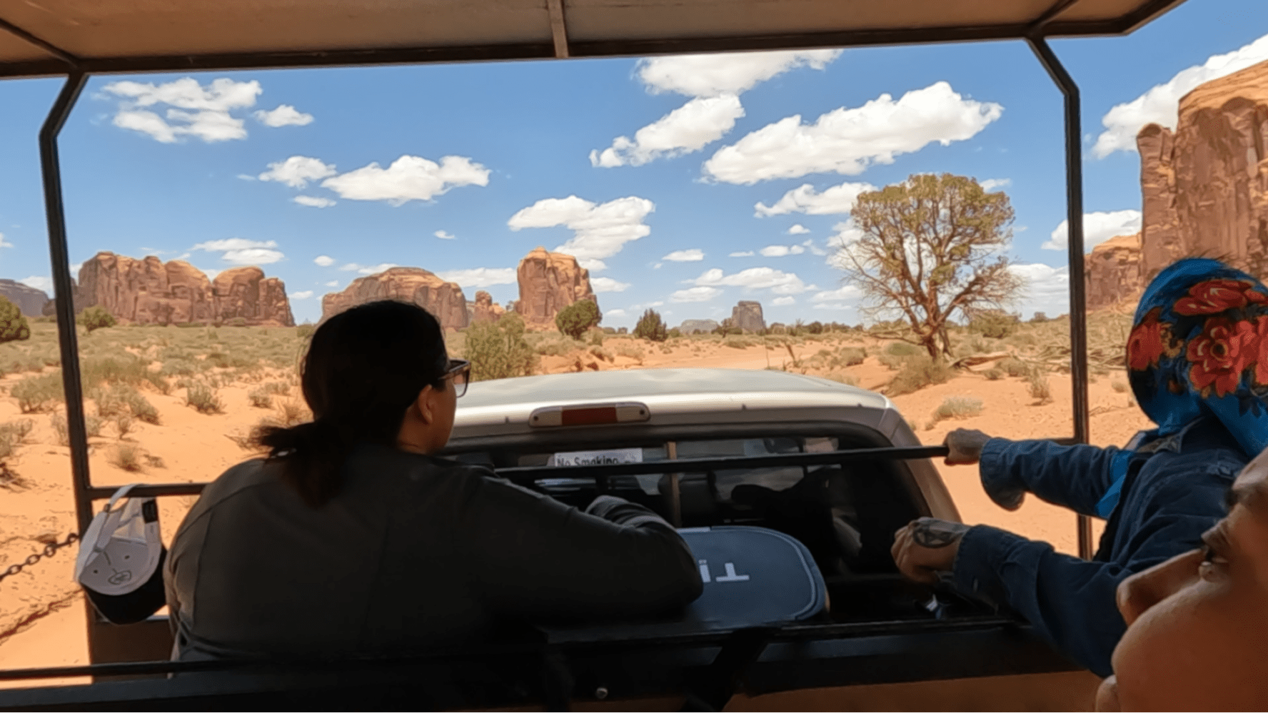 People in a vehicle on a desert tour with rock formations and blue sky.