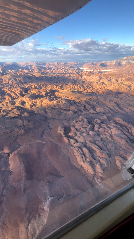 View from airplane window of rocky desert landscape with clouds.