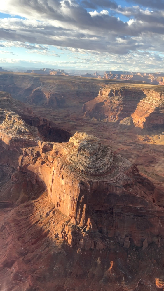 Aerial view of rocky canyon landscape with red cliffs and scattered clouds.